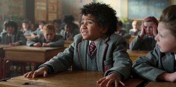 Movie still from “Roald Dahl's Matilda the Musical” (2022), directed by Matthew Warchus – A boy in a school uniform sitting at a desk; Close Up shot, High angle