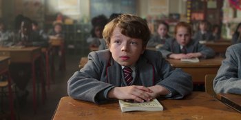 Movie still from “Roald Dahl's Matilda the Musical” (2022), directed by Matthew Warchus – A young boy sitting at a table with a book; Close Up shot, High angle
