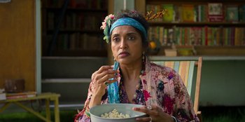 Movie still from “Roald Dahl's Matilda the Musical” (2022), directed by Matthew Warchus – A woman sitting in a chair holding a bowl of popcorn; Close Up shot, Over the shoulder angle