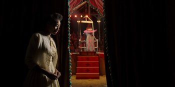 Movie still from “Roald Dahl's Matilda the Musical” (2022), directed by Matthew Warchus – A woman standing in front of a stage with a clown on it; Medium shot, Low angle