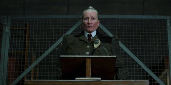 Movie still from “Roald Dahl's Matilda the Musical” (2022), directed by Matthew Warchus – An old man in a uniform is sitting at a podium; Close Up shot, Low angle