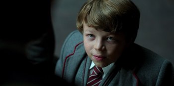 Movie still from “Roald Dahl's Matilda the Musical” (2022), directed by Matthew Warchus – A young boy in a suit and tie looking into the camera; Close Up shot, High angle
