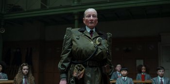 Movie still from “Roald Dahl's Matilda the Musical” (2022), directed by Matthew Warchus – An old man in a military uniform is holding a cell phone; Medium shot, Low angle