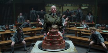 Movie still from “Roald Dahl's Matilda the Musical” (2022), directed by Matthew Warchus – An older man standing in front of a large chocolate cake; Wide shot, Overhead angle