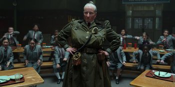 Movie still from “Roald Dahl's Matilda the Musical” (2022), directed by Matthew Warchus – A woman in a trench coat standing in front of a group of people; Medium shot, Low angle