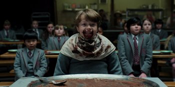 Movie still from “Roald Dahl's Matilda the Musical” (2022), directed by Matthew Warchus – A boy with a bib around his neck eating a cake; Medium shot, High angle