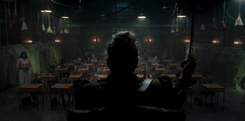 Movie still from “Roald Dahl's Matilda the Musical” (2022), directed by Matthew Warchus – A man sitting in front of an audience in a dark room; Wide shot, High angle