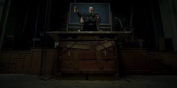 Movie still from “Roald Dahl's Matilda the Musical” (2022), directed by Matthew Warchus – A man sitting on top of a wooden box holding a remote control; Wide shot, Low angle