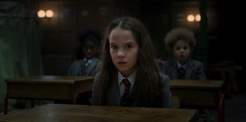 Movie still from “Roald Dahl's Matilda the Musical” (2022), directed by Matthew Warchus – A girl in a suit and tie sitting at a table; Close Up shot, Low angle