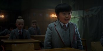 Movie still from “Roald Dahl's Matilda the Musical” (2022), directed by Matthew Warchus – A young boy in a suit and tie in front of a table; Close Up shot, Low angle