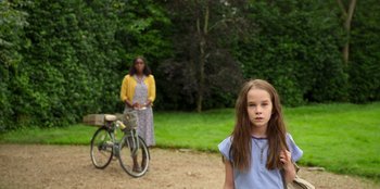 Movie still from “Roald Dahl's Matilda the Musical” (2022), directed by Matthew Warchus – A woman and a girl standing in front of a bicycle; Wide shot, Over the shoulder angle