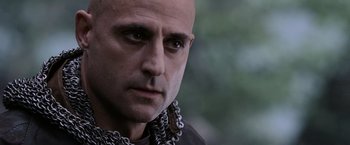 Movie still from “Robin Hood” (2010), directed by Ridley Scott – A bald man wearing chains looking at the camera; Close Up shot, Over the shoulder angle