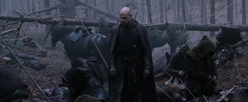 Movie still from “Robin Hood” (2010), directed by Ridley Scott – A bald man in a black cape and a black cape; Medium shot, Over the shoulder angle