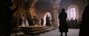 Movie still from “Robin Hood” (2010), directed by Ridley Scott – A group of people standing in front of a stone building; Wide shot, Low angle