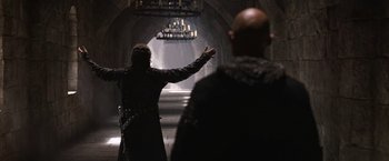 Movie still from “Robin Hood” (2010), directed by Ridley Scott – A man in a black jacket is pointing to the ceiling; Wide shot, Low angle