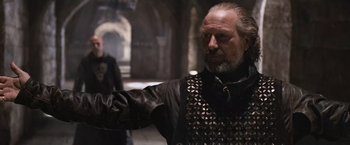 Movie still from “Robin Hood” (2010), directed by Ridley Scott – An older man in a leather jacket and a leather vest; Close Up shot, Low angle