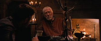 Movie still from “Robin Hood” (2010), directed by Ridley Scott – An older man sitting at a table in front of candles; Medium shot, Over the shoulder angle