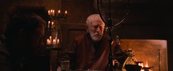 Movie still from “Robin Hood” (2010), directed by Ridley Scott – An older man sitting at a table with a glass of wine; Medium shot, High angle
