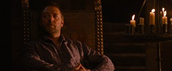 Movie still from “Robin Hood” (2010), directed by Ridley Scott – A man sitting in a chair with his arms crossed; Medium shot, Low angle