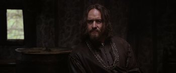 Movie still from “Robin Hood” (2010), directed by Ridley Scott – A man with long hair and a beard wearing chains; Medium shot, Over the shoulder angle