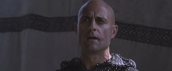 Movie still from “Robin Hood” (2010), directed by Ridley Scott – A bald man in chain mail looking at the camera; Close Up shot, Low angle