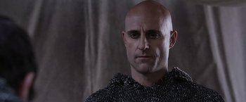 Movie still from “Robin Hood” (2010), directed by Ridley Scott – A bald man in chain mail is looking at the camera; Close Up shot, Low angle