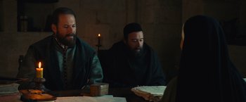 Movie still from “Benedetta” (2021), directed by Paul Verhoeven – Two men sitting at a table with a candle in the background; Medium shot, Over the shoulder angle