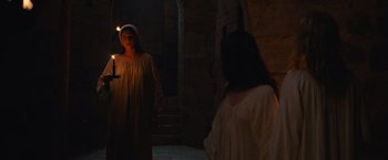 Movie still from “Benedetta” (2021), directed by Paul Verhoeven – Two women in medieval garb are standing in the dark; Medium shot, Over the shoulder angle