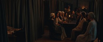 Movie still from “Benedetta” (2021), directed by Paul Verhoeven – A group of people sitting around a table with a lit candle; Wide shot, High angle