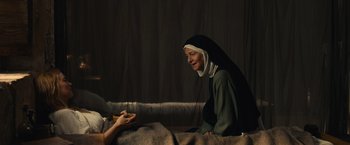 Movie still from “Benedetta” (2021), directed by Paul Verhoeven – A nun sitting next to a person holding a piece of food; Medium shot, Over the shoulder angle