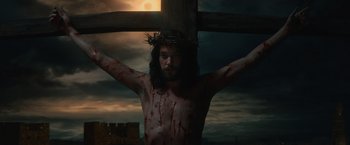 Movie still from “Benedetta” (2021), directed by Paul Verhoeven – A man with a crown of thorns on his head holding a wooden cross; Medium shot, Low angle