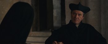 Movie still from “Benedetta” (2021), directed by Paul Verhoeven – A man wearing a black hat and a black coat; Close Up shot, Over the shoulder angle
