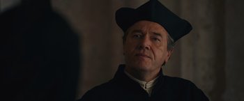 Movie still from “Benedetta” (2021), directed by Paul Verhoeven – An older man wearing a black hat looking to his left; Close Up shot, Over the shoulder angle
