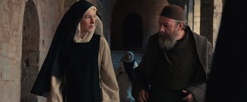 Movie still from “Benedetta” (2021), directed by Paul Verhoeven – A nun and a man are walking in a building; Medium shot, Low angle