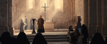 Movie still from “Benedetta” (2021), directed by Paul Verhoeven – A priest standing in front of a cross in a church; Wide shot, Low angle