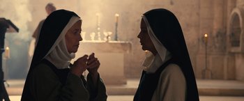 Movie still from “Benedetta” (2021), directed by Paul Verhoeven – Two women are standing in a room and one is holding a rosary and the other is holding a candle; Close Up shot, Over the shoulder angle