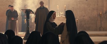 Movie still from “Benedetta” (2021), directed by Paul Verhoeven – A woman in a nun's outfit is putting ashes in her mouth; Medium shot, Over the shoulder angle