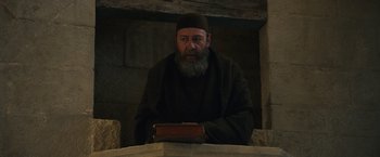 Movie still from “Benedetta” (2021), directed by Paul Verhoeven – An old man with a beard and a hat is holding a book; Medium shot, Low angle