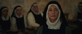 Movie still from “Benedetta” (2021), directed by Paul Verhoeven – Two women dressed in black and white are standing in front of a stone wall; Close Up shot, Over the shoulder angle