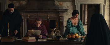 Movie still from “Benedetta” (2021), directed by Paul Verhoeven – A man and a woman sitting in front of a fireplace; Medium shot, Low angle
