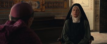 Movie still from “Benedetta” (2021), directed by Paul Verhoeven – An older woman sitting in front of an older man; Medium shot, Over the shoulder angle