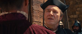 Movie still from “Benedetta” (2021), directed by Paul Verhoeven – An older man wearing a black hat and a red shirt; Close Up shot, Over the shoulder angle