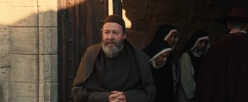 Movie still from “Benedetta” (2021), directed by Paul Verhoeven – An older man with a beard wearing a monk's outfit; Medium shot, Over the shoulder angle