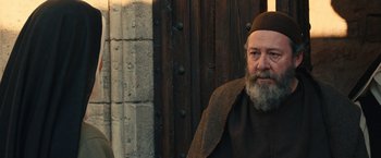 Movie still from “Benedetta” (2021), directed by Paul Verhoeven – An older man with a long beard wearing a cap; Medium shot, Over the shoulder angle