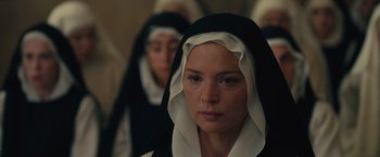 Movie still from “Benedetta” (2021), directed by Paul Verhoeven – A woman in a black and white dress with a nun in the background; Close Up shot, High angle
