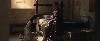 Movie still from “Benedetta” (2021), directed by Paul Verhoeven – A man and a woman sitting on a bed in a room; Wide shot, High angle