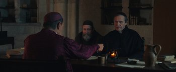 Movie still from “Benedetta” (2021), directed by Paul Verhoeven – A group of men sitting at a table with a candle; Medium shot, Over the shoulder angle