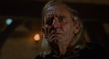 Movie still from “Robin Hood: Prince of Thieves” (1991), directed by Kevin Reynolds – An old man with long hair and a goatee stares into the camera; Close Up shot, Low angle