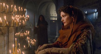 Movie still from “Robin Hood: Prince of Thieves” (1991), directed by Kevin Reynolds – A woman sitting next to a tree in a room with candles; Medium shot, Over the shoulder angle
