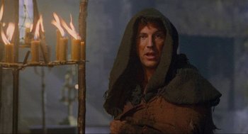 Movie still from “Robin Hood: Prince of Thieves” (1991), directed by Kevin Reynolds – A man in a hooded jacket standing in front of candles; Close Up shot, Low angle